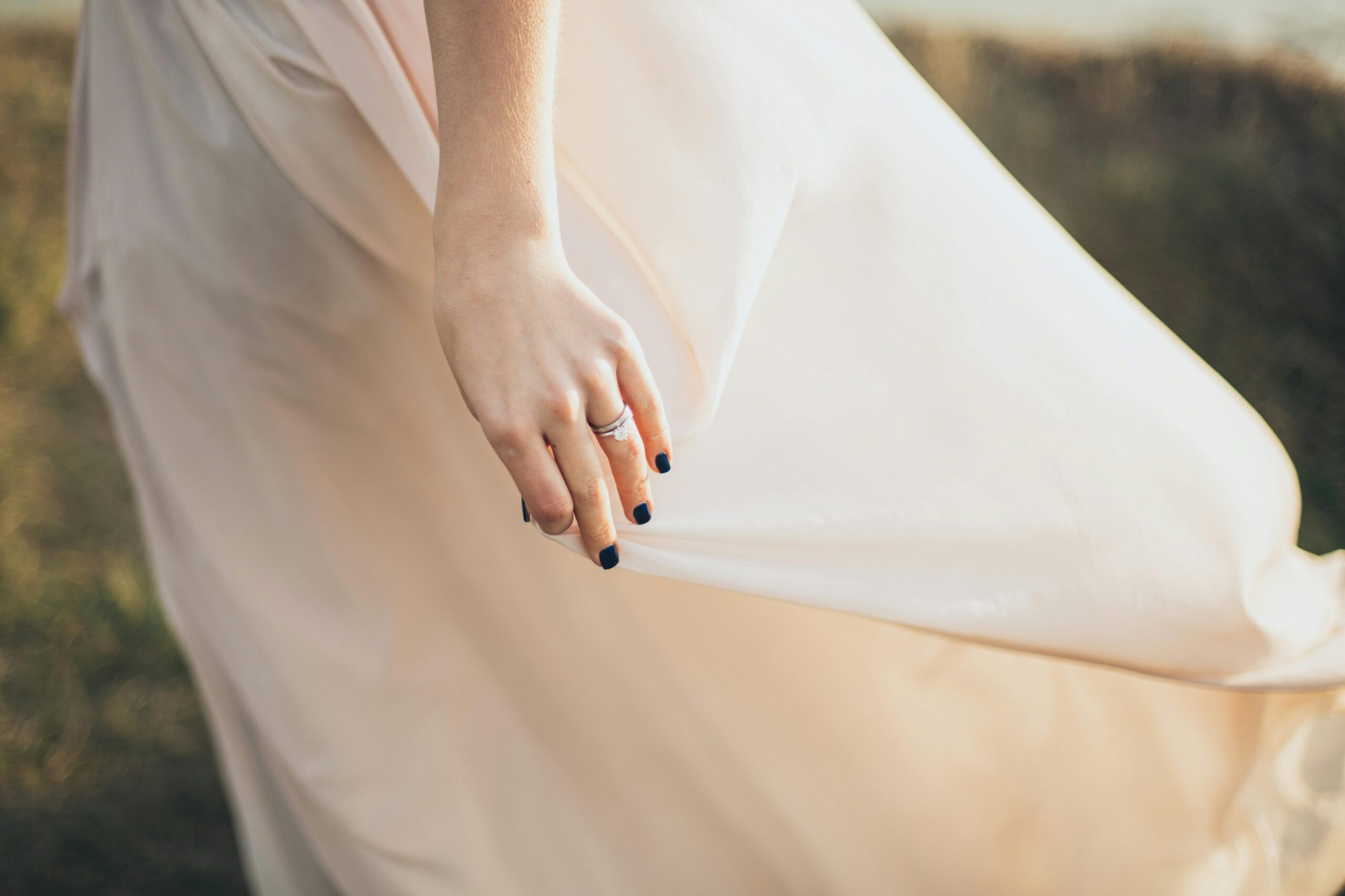 Close-up of a bride holding her wedding dress outdoors, showcasing elegance and style.