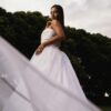 Beautiful bride posing in a white gown, showcasing elegance and grace against lush green trees.