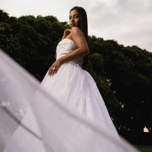 Beautiful bride posing in a white gown, showcasing elegance and grace against lush green trees.