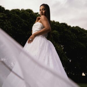 Beautiful bride posing in a white gown, showcasing elegance and grace against lush green trees.
